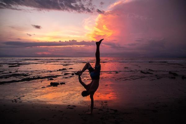 CANOPI Covering Equipping Uniting man doing handstand on beach in sunset
